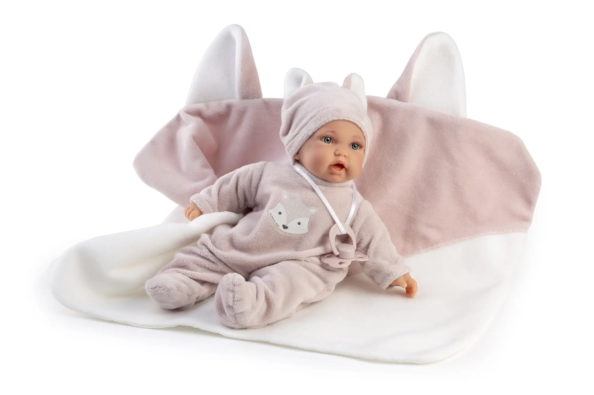 Muñeca Petit Blandito con Manta Zorrito sentada delante de la manta abierta, con conjunto rosa, gorro de orejas y chupete colgado.