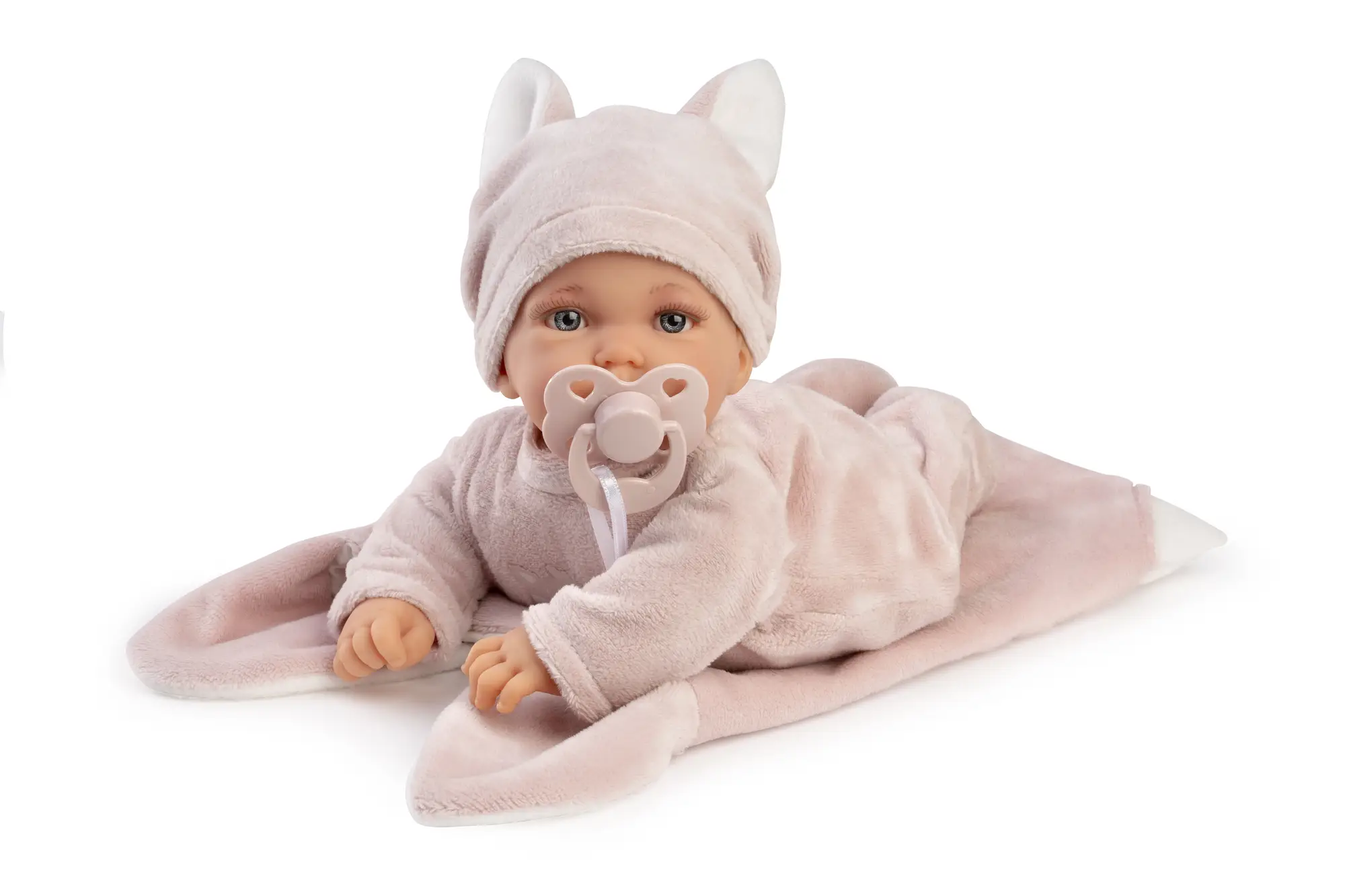 Muñeca Petit Blandito tumbada boca abajo sobre la manta rosa, con gorro de orejas y chupete.