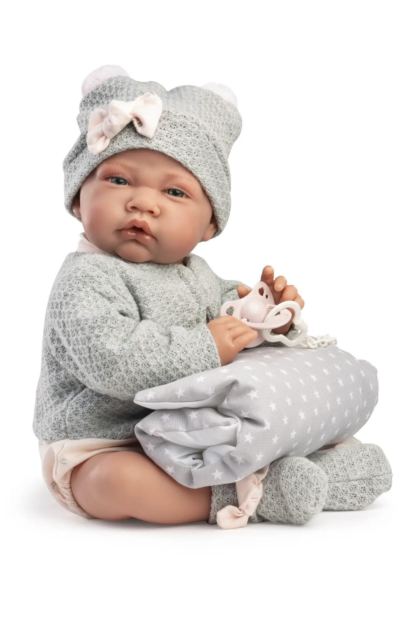 Muñeca Recién Nacida Lúa sentada con conjunto gris, sosteniendo el cojín de estrellas y el chupete entre las manos.
