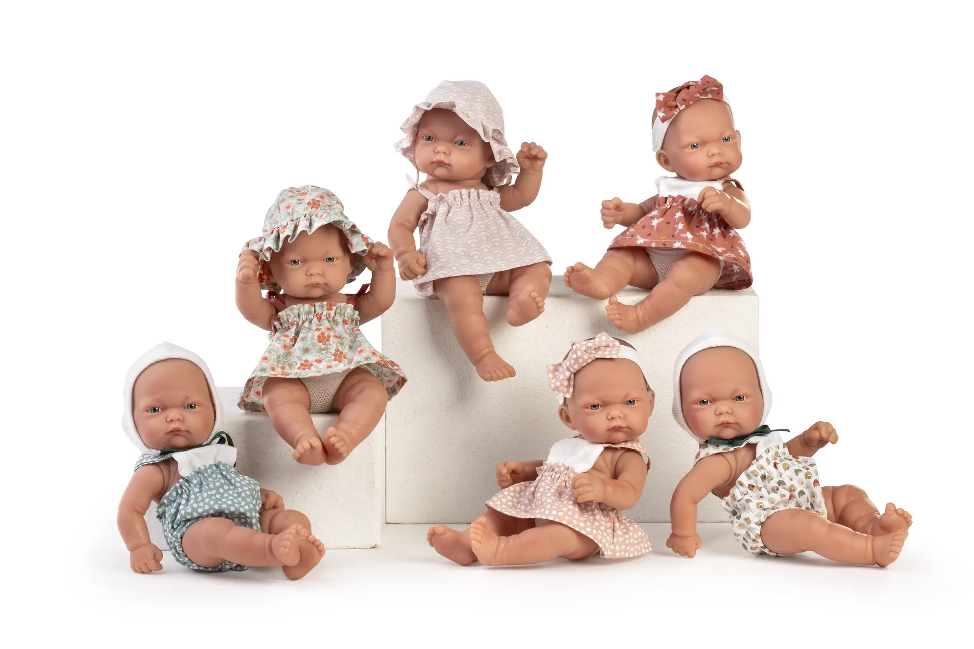 Colección de Muñecas Pitu Antonio Juan Siete muñecas Pitu Antonio Juan sentadas en grupo con vestidos, gorros y lazos de distintos estampados.