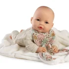 Muñeca Bimba Lloro Orejitas apoyada boca abajo sobre una manta blanca, con conjunto beige y babero floral.