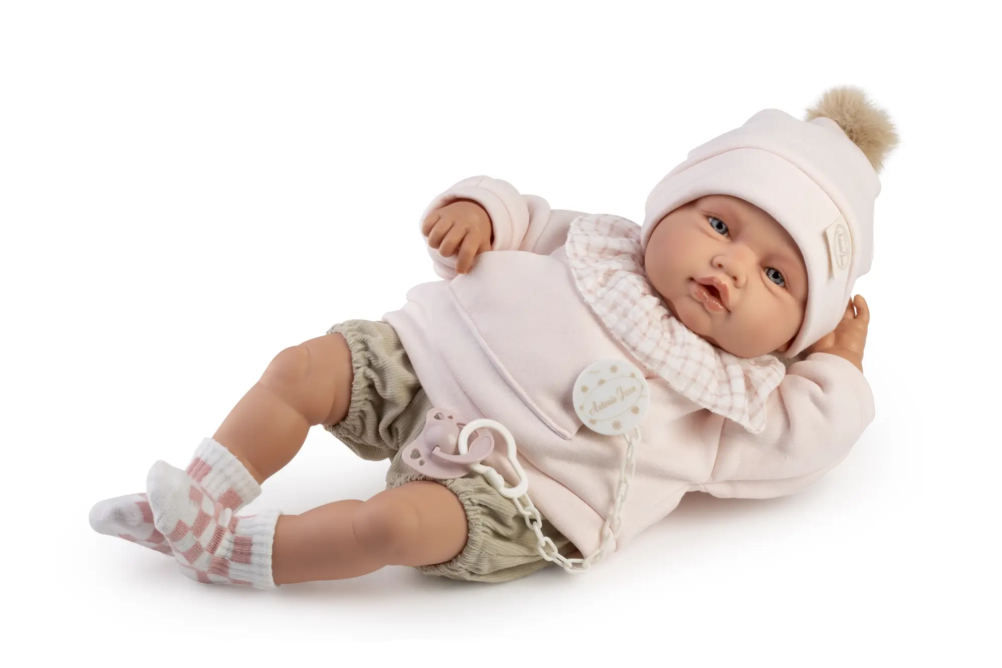 Muñeco Babydoo Posturitas Urban de Antonio Juan recostado de lado, con gorro de pompón, conjunto rosa y gris, calcetines de cuadros y chupete.