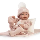 Muñeca Recién Nacida Pipa de Antonio Juan sentada sobre una colcha rosa junto a un cojín blanco, con conjunto de punto y gorro con pompón.