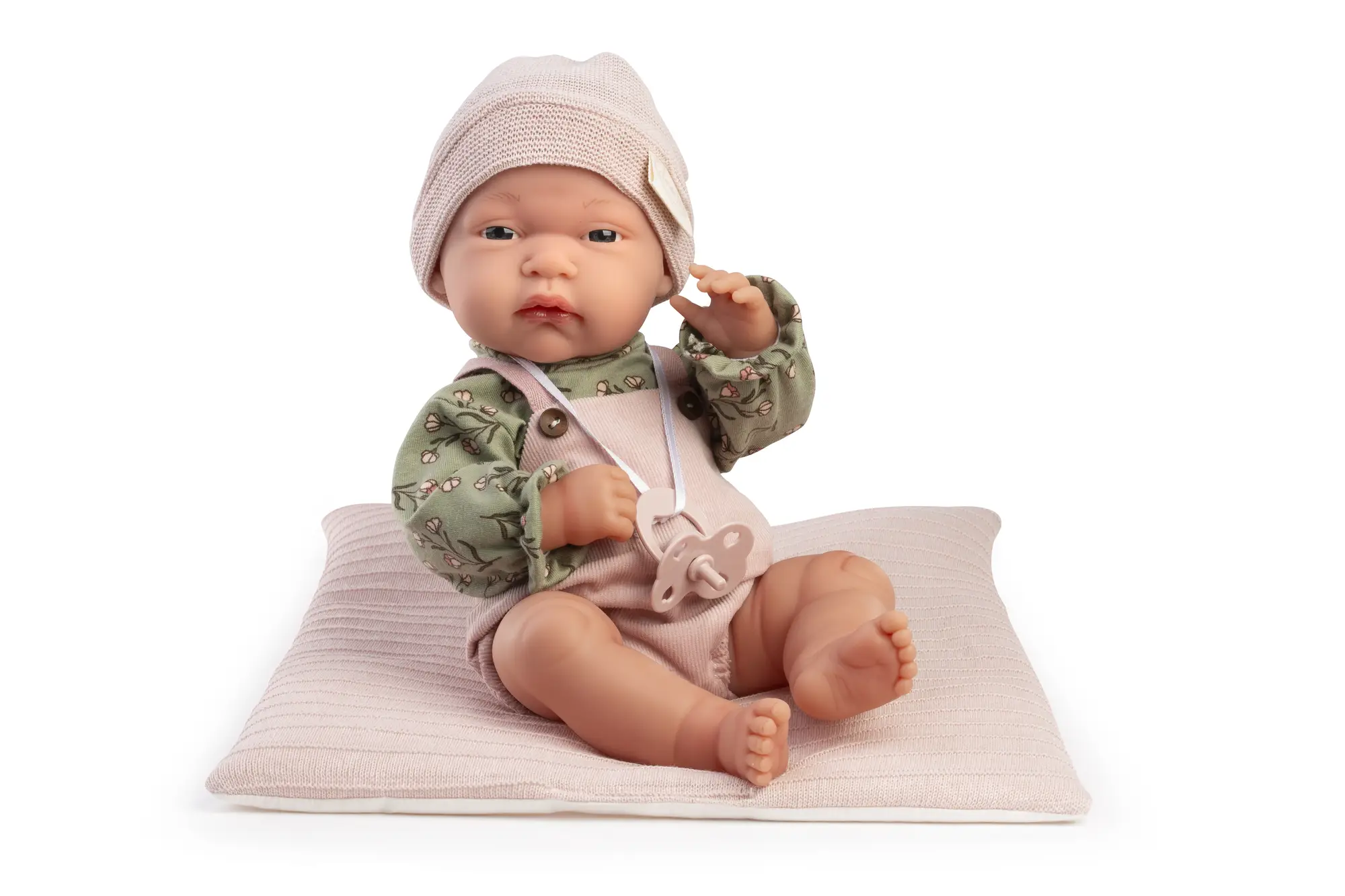 Muñeca Baby Toneta Pana sentada sobre un cojín rosa con gorro, blusa verde de flores, peto y chupete colgado.