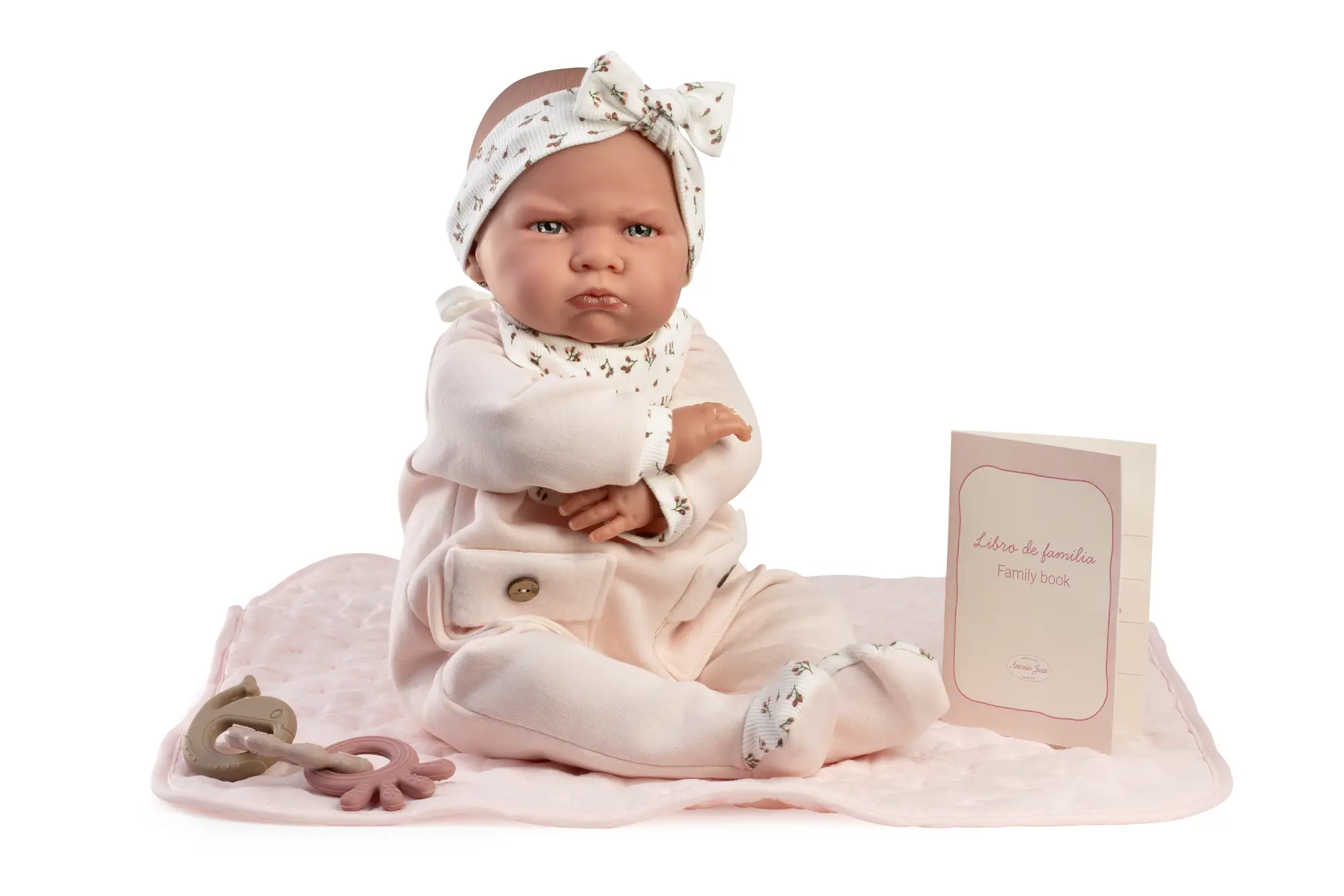 Mi Primer Reborn Berta Antonio Juan con manta Muñeca Mi Primer Reborn Berta de Antonio Juan sentada sobre una manta rosa, con conjunto floral, lazo y libro de familia.