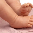 Primer plano de los pies de la muñeca Reborn Baby Love apoyados sobre una manta de punto rosa.