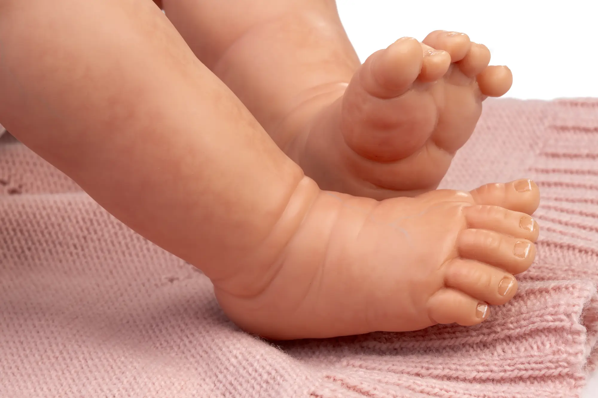 Primer plano de los pies de la muñeca Reborn Baby Love apoyados sobre una manta de punto rosa.